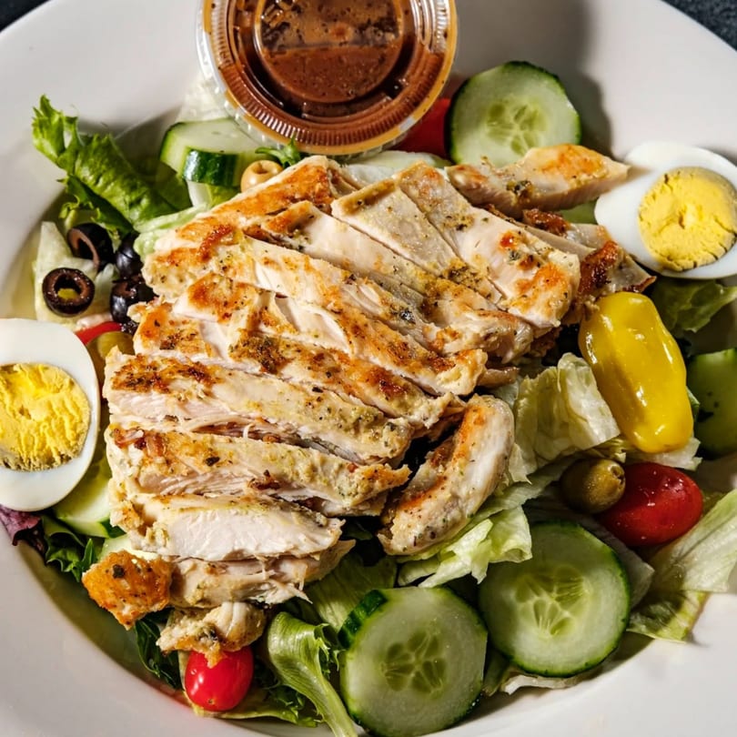 Grilled chicken salad with lettuce, cucumbers, tomatoes, olives, hard-boiled eggs, and dressing.
