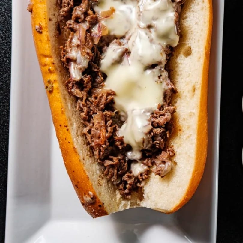 A close-up of a Beto’s cheesesteak sandwich with melted cheese and steak on a white plate.