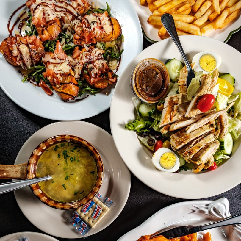 An overhead view of Beto's Italian dishes, including bruschetta, chicken salad, soup, and french fries.