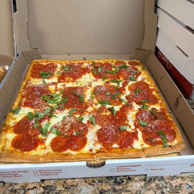 A square pepperoni pizza with fresh basil and parmesan cheese in a Beto's pizza box.