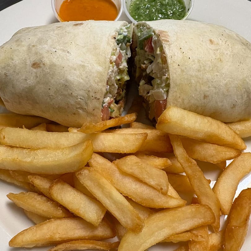 A large, sliced burrito filled with vegetables and sauce, served with a side of golden french fries.