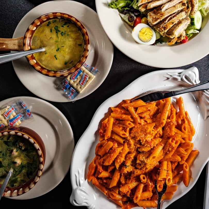 Top-down view of Beto's Italian dishes: penne pasta, two soups, and a grilled chicken salad.